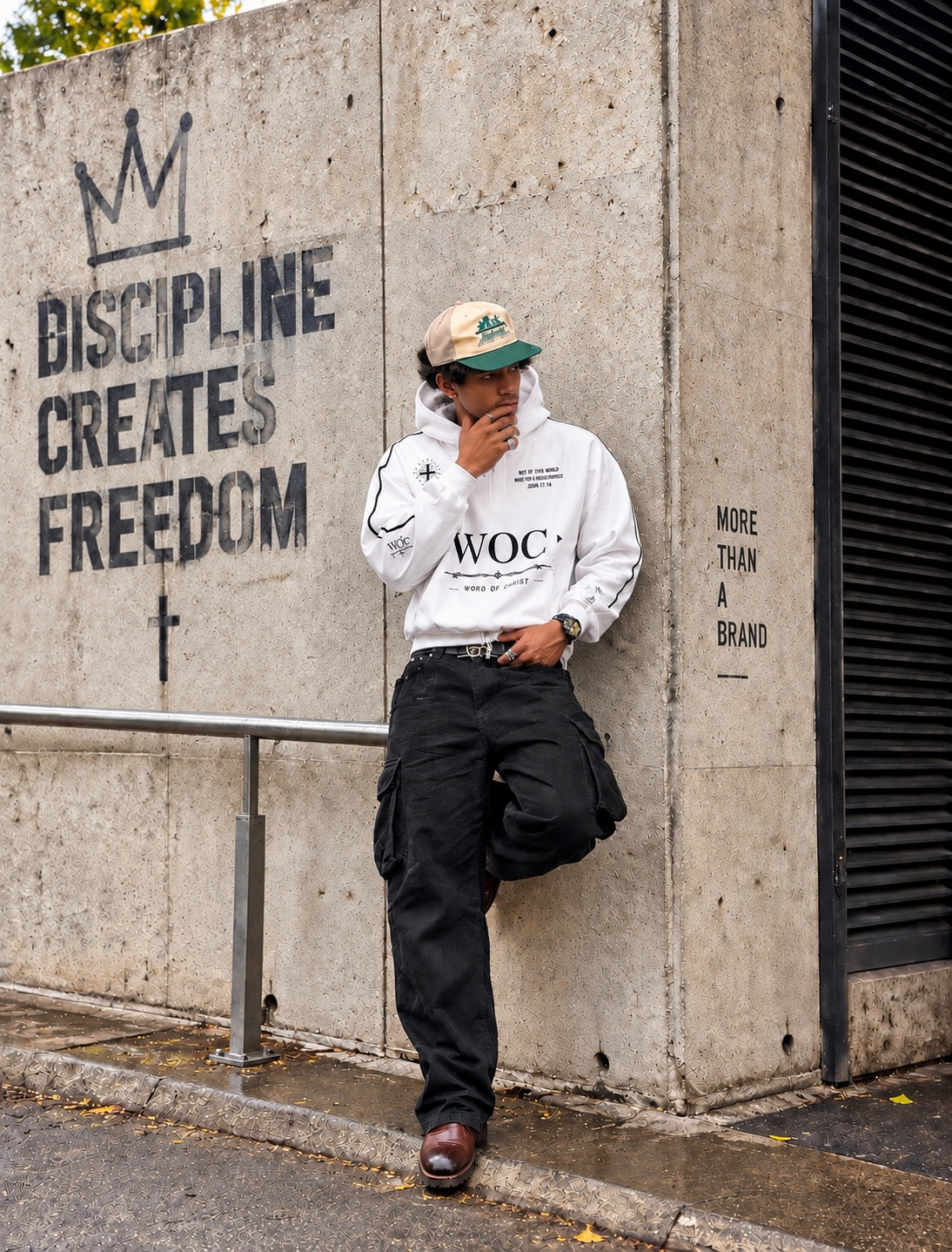 Model wearing a white WOC hoodie beside a concrete wall